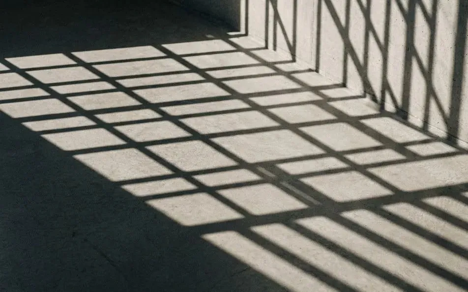 Hard window shadows falling across a concrete wall in a grid